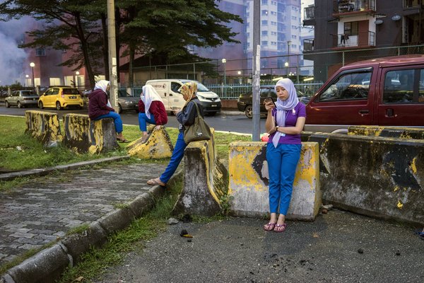 A group of young Indonesian migrant workers take a break to check their phones after getting off work at a nearby hi-tech factory facility in Malaysia. Staton Winter for UN Women. CC BY-NC-ND.